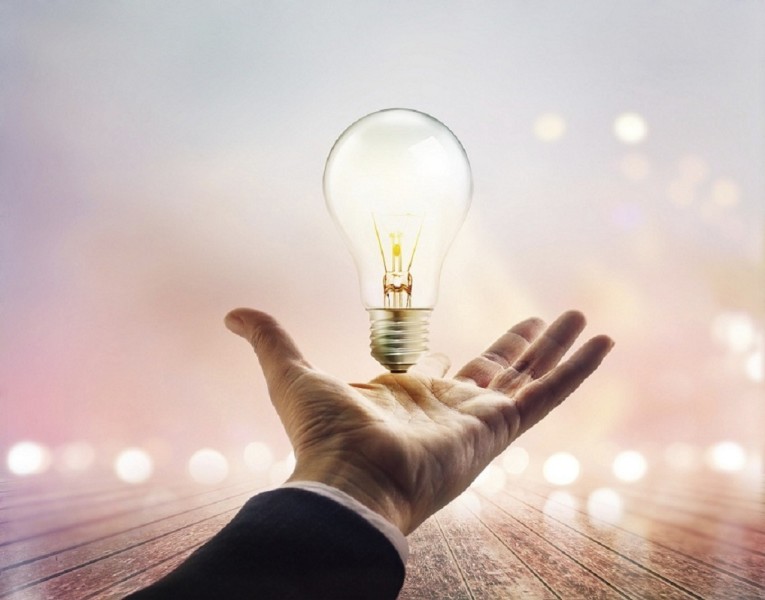 Hands of a businessman reaching to towards light bulb on wooden